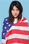 Patriotic young woman wrapped in American flag over blue background