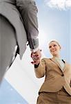 Businessman and businesswoman shaking hands under blue sky