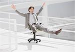 Carefree businessman sliding down walkway on office chair with wheels