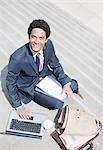 Portrait of smiling businessman with paperwork using laptop on sunny stairs