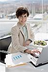 Portrait of smiling businesswoman eating lunch and working at desk