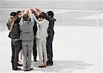 Business people standing in huddle with arms raised