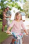 Portrait of smiling girl on bicycle with parents in background