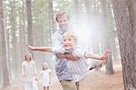 Father flying son in sunny woods