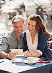 Smiling couple looking at postcard at sidewalk cafe