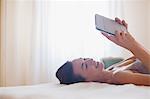 Smiling woman laying on bed and using digital tablet