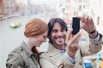 Laughing couple taking self-portrait with camera phone on canal in Venice