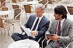 Smiling businessmen with digital tablet and paperwork in cafe