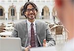 Smiling businessman talking to co-worker at sidewalk cafe