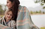 Portrait of smiling daughter wrapped in blanket with mother at lakeside