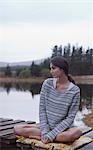 Pensive woman sitting on dock at lake