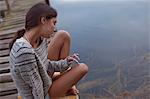 Pensive woman sitting on dock over lake