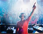 Portrait of enthusiastic DJ with arm raised and people on dance floor in background