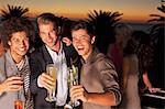 Portrait of smiling men toasting cocktails on balcony at sunset