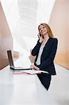 Smiling businesswoman talking on cell phone and using laptop in office