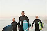 Older surfers carrying boards on beach