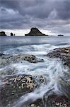 Waves swirl around the rocky seashore of Vagar, looking towards the beautiful island of Tindholmur in the Faroe Islands, Denmark, Europe