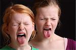 Two girls showing their tongues on black background