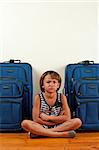 A young girl sits in front of suitcases, with a sad expression on her face.