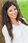 Outdoor portrait of a beautiful young Latina Hispanic woman smiling leaning against a tree