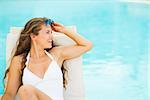 Happy young woman in swimsuit on chaise-longue and looking on copy space