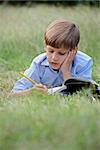 Young people and education, school child doing homework, laying down on grass at park and studying with book. Medium shot, copy space