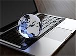3D image of modern laptop and crystal globe on wooden desk
