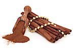 Cinnamon sticks and powder in an olive wood scoop with gold bead chain over white background.