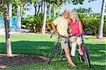 Happy senior man and woman couple together cycling on bicycles in a sunny green tropical park