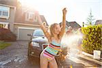 Young girl dances while family washes car in the driveway of their home on a sunny summer afternoon in Portland, Oregon, USA