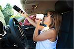 Young girl applying lip gloss pretending to be old enough to drive as her smiling father watches on on a sunny summer evening in Portland, Oregon, USA