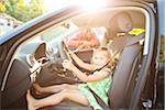 Little girl sitting in driver's seat of car wearing seatbelt, pretending to be old enough to drive and showing she knows the importance of a seat belt as her smiling father watches on on a sunny summer evening in Portland, Oregon, USA