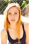 Close-up portrait of young woman standing in front of chain link fence in park near the tennis court on a warm summer day in Portland, Oregon, USA