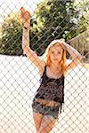 Portrait of young woman standing behind chain link fence in park near the tennis court on a warm summer day in Portland, Oregon, USA