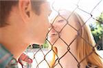 Young couple kissing through chain link fence in park near the tennis court on a warm summer day in Portland, Oregon, USA