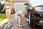 Sisters washing car in the driveway of their home on a sunny summer afternoon in Portland, Oregon, USA