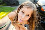 Portrait of young girl sticking her tongue out while washing car in the driveway of their home on a sunny summer afternoon in Portland, Oregon, USA