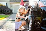 Young daughter helps father wash their car in the driveway of their home on a sunny summer afternoon in Portland, Oregon, USA