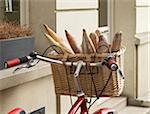 Close-up of fresh baguettes in wicker basket attached to handlebars of red, classic, road bicycle, Paris, France