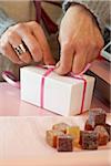 Close-Up of Woman's Hands Tying Bow on Small White Gift Box in Shop, with Candies in Foreground, Paris, France