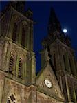 Moon above moss covered church towers with clock at night, Sarrebourg, France