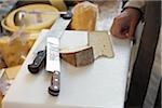 shopkeeper cutting fresh wedges of French goat cheese in artisan cheese shop with knives on cutting board, La Fromagerie, Paris, France