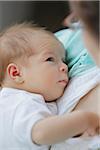 newborn baby girl in a white undershirt in the arms of her mother looking up into her eyes