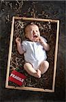 yawning newborn baby girl wearing white undershirt onesie in a shipping box labeled as fragile with packing paper