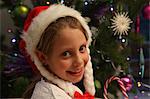 Girl wearing Santa hat by Christmas tree