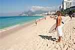 South America, Rio de Janeiro, Rio de Janeiro city, Ipanema, surfer with a surf board looking out over the Atlantic from the Arpoador on Ipanema beach with the Dois Irmaos mountains in the distance