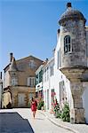France, Charente Maritime, Ile de Re.  Tourist walks along a quiet cobbled street leading off the village square in Ars en Re. MR
