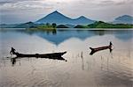 Young boys fish from dugout canoes on Lake Mutanda with its stunning backdrop of the Virunga Volcanoes, Uganda, Africa