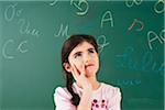 Girl Looking up and Thinking in front of Chalkboard in Classroom