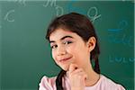 Girl with Hand on Chin in Front of Chalkboard in Classroom